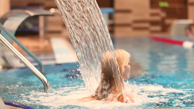Spa guest enjoys hydro massage waterfall jet in indoor pool