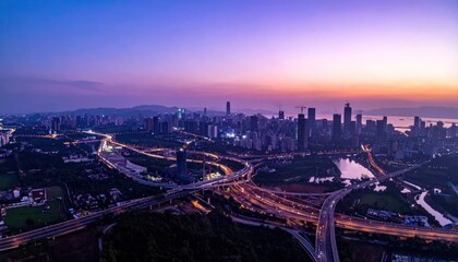 Obraz premium Panoramic aerial view of a vibrant city skyline at dusk, featuring intricate highway interchanges and illuminated skyscrapers.