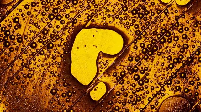 Golden liquid forming a question mark symbol surrounded by bubbling oil and water in a macro shot