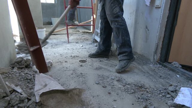 Unrecognizable builder collecting construction debris with a shovel. House renovation.   Worker picking up masonry debris with shovel after demolition
