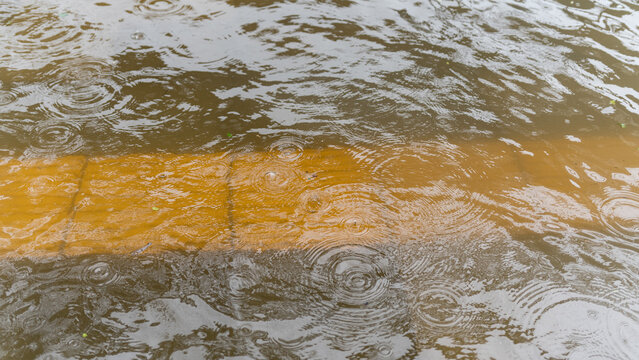 Heavy rain falling on a flooded street with a visible yellow road marking under murky water