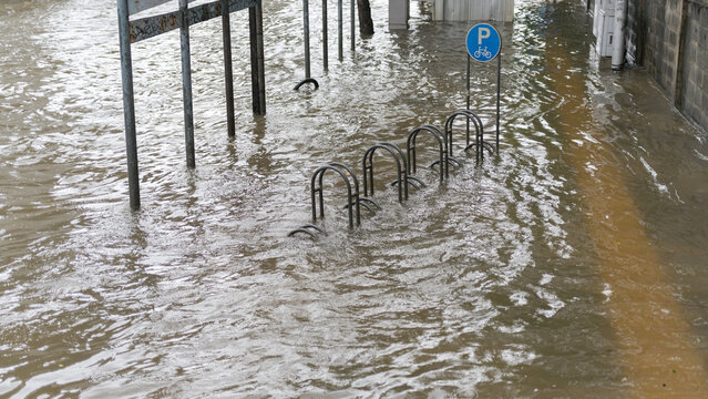 Urban street flooding submerging a bicycle parking rack and a blue parking sign in city water