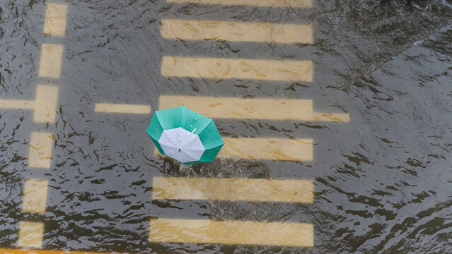 Aerial view of a person walking with a green umbrella across a flooded city street crosswalk