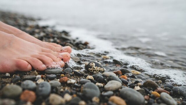 Close-up of toes on pebble beach with gentle waves lapping shoreline