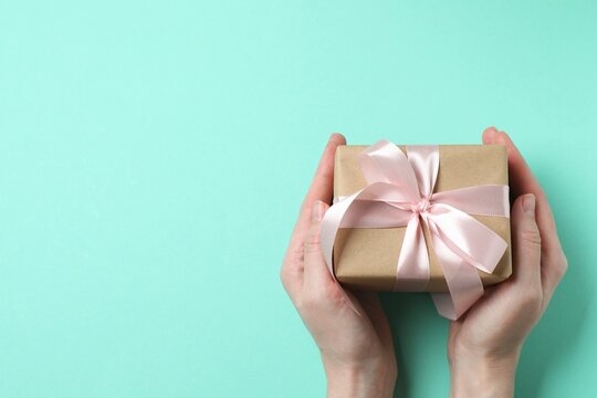 Woman holding gift box with pink bow on pastel background, top view