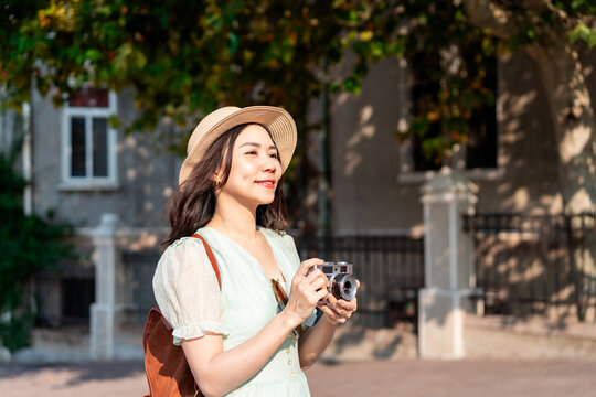 Happy young Asian woman tourist holding a camera enjoying travel photography and city exploration
