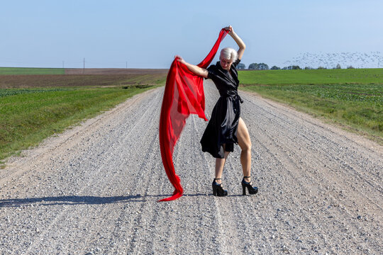 Elegant woman in a black dress and red scarf posing gracefully on a country road