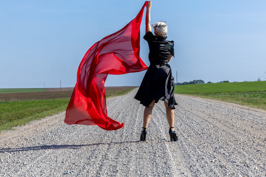 Elegant woman in a black dress and red scarf posing gracefully on a country road
