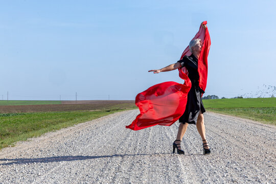 Elegant woman in a black dress and red scarf posing gracefully on a country road