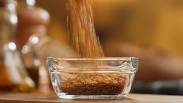 Flax seeds in wooden spoon and bowl macro close up, golden and brown linseed grains falling, raw flaxseed healthy omega 3 superfood ingredient texture