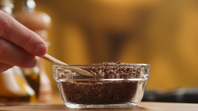 Flax seeds in wooden spoon and bowl macro close up, golden and brown linseed grains falling, raw flaxseed healthy omega 3 superfood ingredient texture