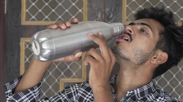 Young man drinking water from a steel bottle indoors