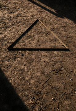 Geometry and minimalism concept, metal triangle frame placed on dry earth ground with harsh sunlight and shadows in an outdoor natural environment