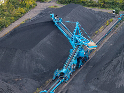Aerial view of a large blue stacker machine operating on a massive coal pile at an industrial mining site in Berlin, Berlin, Germany.