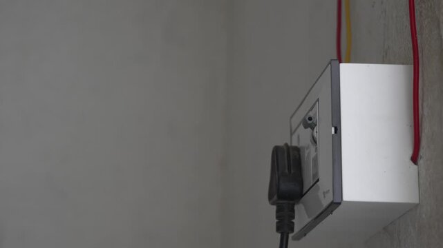 Electrician hand plugging cable into wall socket unit