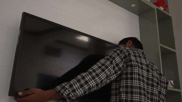 Technician mounting television screen on wall bracket indoors