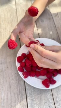  Close-up of a child putting fresh raspberries on fingers like thimbles