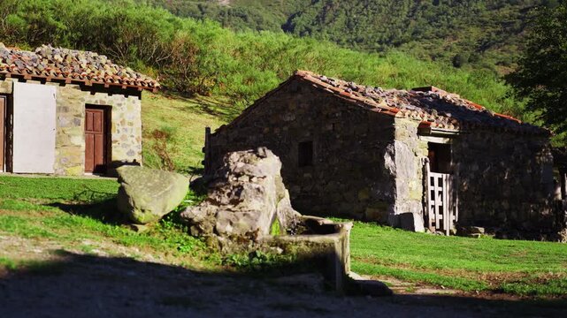 Old stone houses with a stone water trough and a fountain in a rural mountain landscape with green hills, symbolizing a simple and tranquil country lifestyle