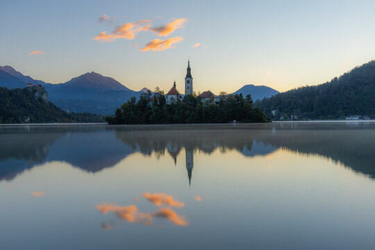 View of Lake Bled with the Pilgrimage Church of the Assumption of Maria on the island, reflected in the calm water at sunrise with mountains in the background, Bled, Radovljica, Slovenia.