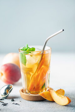 Fruit black iced tea with peaches and mint in a glass on the table. Summer drink concept