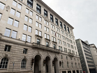 Obraz premium Historic office building facade in Liverpool UK with classical stone architecture, arched entrances, corporate windows and flag on an overcast city street