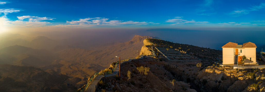 View of Gorakh Hill Station at sunset, featuring a building perched on a rocky mountain ridge overlooking the vast, hazy landscape of Gorakh Hill, Sindh, Pakistan.