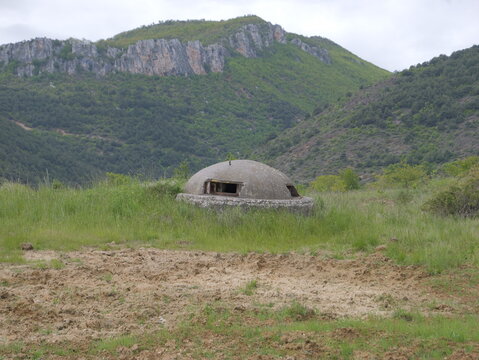 View of a concrete bunker situated in a grassy field with rugged mountains in the background in Pogradec, Korce County, Albania.