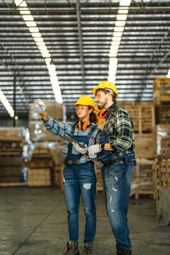 A female engineer pointing down the aisle and a bearded coworker mapping a forklift route in a large warehouse during a process research study for robotic automation