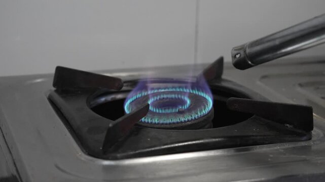 Person igniting a gas stove burner with a lighter in a kitchen