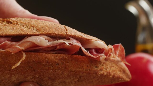Sandwich with jamon serrano and iberico, Spanish cured ham bocadillo in crusty baguette, traditional prosciutto ham sandwich close up for breakfast in cafe
