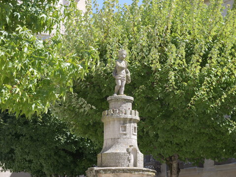 View of the Fonte de Neptuno ou do Anxino, a historic stone fountain featuring a statue of a child, nestled among lush green trees in the city center of Vigo, Pontevedra, Spain.