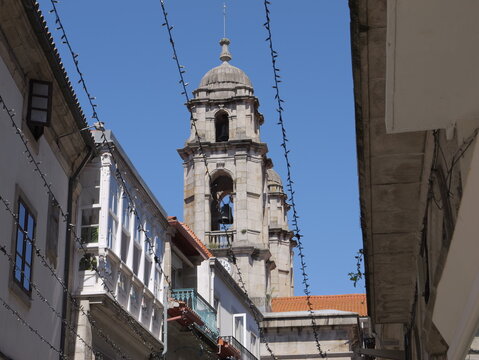 View of the historic bell tower of the Concatedral - Basilica de Santa Maria de Vigo rising above narrow streets with traditional buildings and string lights in Vigo, Pontevedra, Spain.