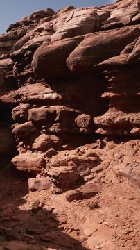 The scene shows various rocks and stone formations in a dry desert area. Sunlight illuminates the textures and colors of the rocks. There is dry earth visible around the stones.