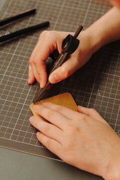 Hands mark leather with a precision divider tool during wallet making. Close-up shows measuring, preparation and skilled artisan craftsmanship.