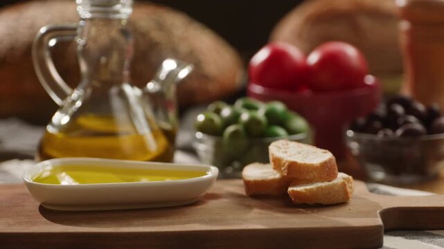 Bread dipping in olive oil close up, hand dips rustic bread into extra virgin olive oil on Mediterranean table with tomatoes and olives, Italian and Spanish food
