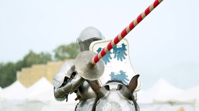 Armored knight sits on horse holding long striped lance. Heavy steel plates protect brave rider preparing for jousting tournament combat under bright sky.