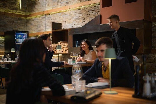 Young couple, African American woman and man, enjoying a chat as waiter serves their food at a busy luxury restaurant.