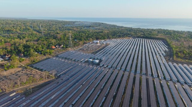 Aerial view of PLTS Bali Timur solar farm featuring extensive rows of photovoltaic panels surrounded by lush greenery and coastal landscape in Kubu, Bali, Indonesia.