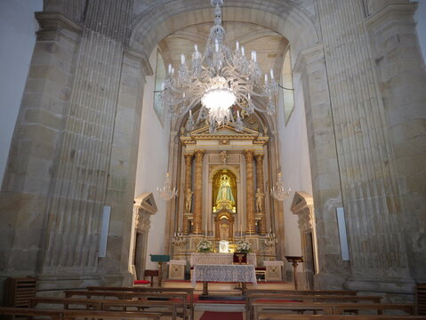 View of the ornate altar and crystal chandelier inside the Santuario de la Virgen Peregrina with wooden pews and stone columns in Pontevedra, Pontevedra, Spain.