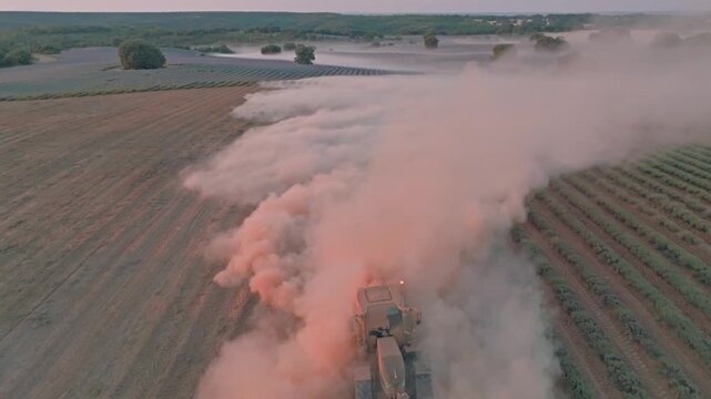 Aerial view of a tractor harvesting lavender fields in Brihuega, creating a large cloud of dust during the golden hour in Brihuega, Castile-La Mancha, Spain.