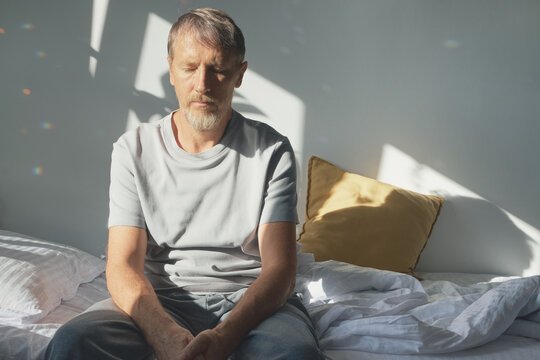 Emotionally exhausted man sitting on bed with eyes closed, thinking about mental health