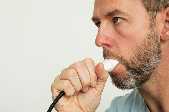 Close-up of a man using a spirometer mouthpiece for lung function diagnostic test, white background