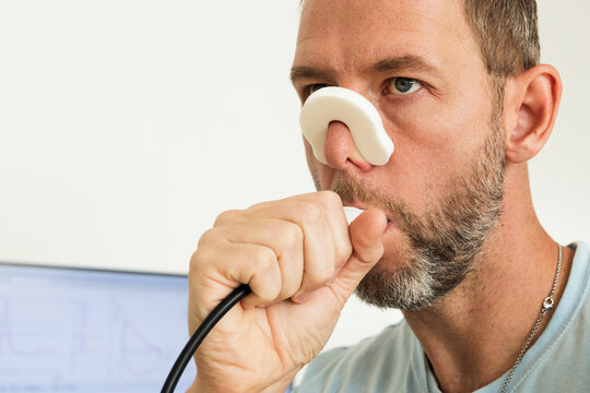 Man doing spirometry lung function test with mouthpiece and nose clip, monitor screen in background