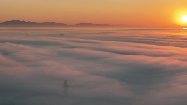 Aerial view of Europa Point lighthouse emerging from thick clouds at sunset with distant mountains on the horizon in Gibraltar, Gibraltar.