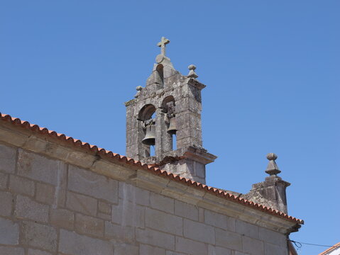 View of Iglesia vella de San Roque with its stone bell gable and bells against a clear blue sky in Combarro, Pontevedra, Spain.