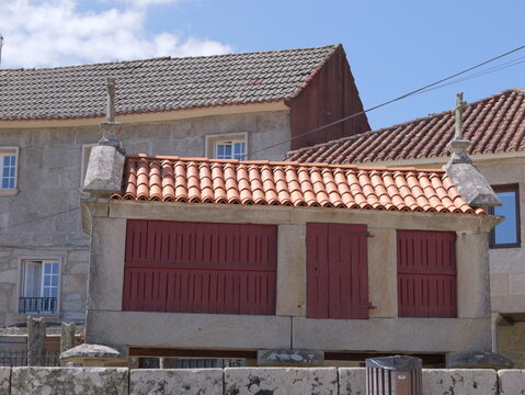 View of a traditional stone horreo with red wooden doors and a tiled roof in the historic village of Combarro, Pontevedra, Spain.
