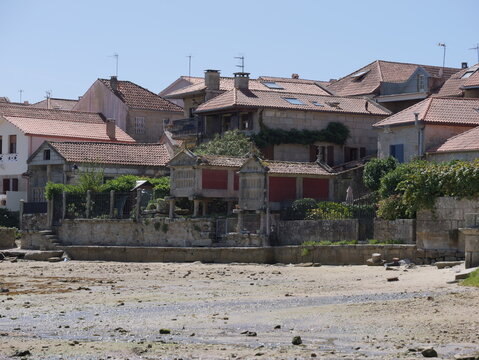 View of traditional stone horreos granaries situated along the waterfront with historic stone houses and terracotta rooftops in Combarro, Pontevedra, Spain.