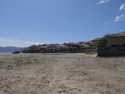 View of the historic coastal village of Combarro with traditional stone granaries lining the waterfront and rocky beach at low tide in Combarro, Pontevedra, Spain.