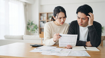 Obraz premium 家計簿や請求書を見ながら家計のやりくりに悩む若い夫婦