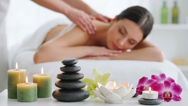 Woman receiving a relaxing back massage in a spa with candles and stones
